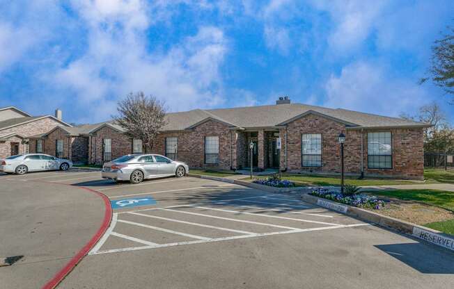 A parking lot in front of a brick building with a car parked in the spot.