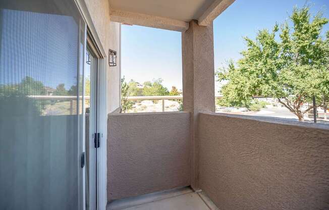 A balcony with a sliding glass door leading to a view of trees and a clear blue sky.