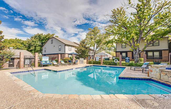 A swimming pool surrounded by a stone patio and a grassy area with trees.