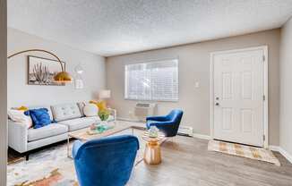 A living room with a white couch, blue chair, and a coffee table at Mountain Vista Apartments, Lakewood, CO, 80228