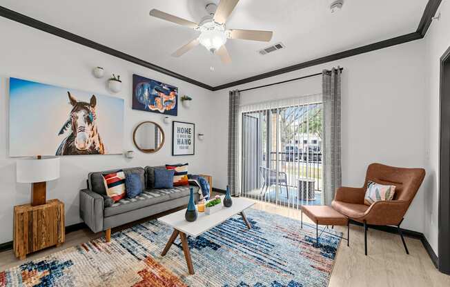 A living room with a grey couch, a brown chair, a wooden table, and a rug with a horse picture on the wall.