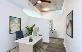 a white desk with a computer in a room with white walls and a ceiling with a fan