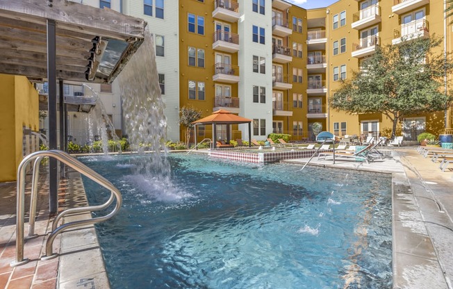 a swimming pool with a waterfall in front of an apartment building