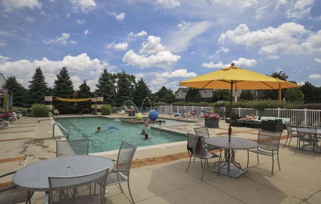 a swimming pool with tables and umbrellas and people in it at Village Club of Rochester Hills, Shelby Township, 48317