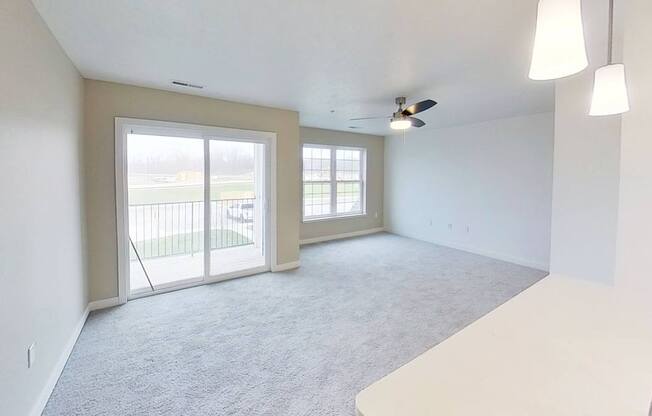A spacious living room with a sliding glass door leading to a balcony at Meadowbrooke Apartment Homes in Kentwood, MI 49512