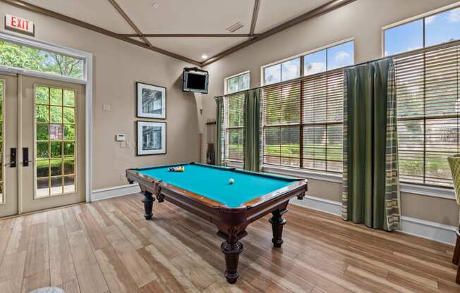 a pool table in club house with windows and a tv