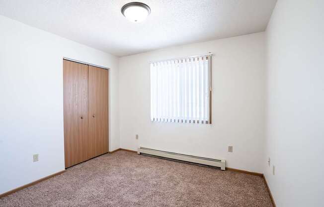 A room with a brown carpet and a window with blinds.