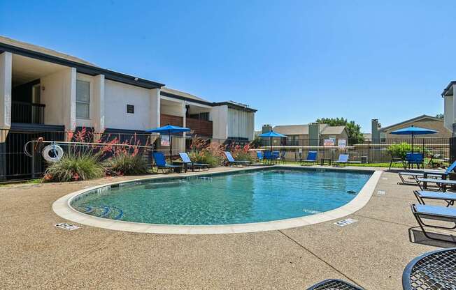 A swimming pool surrounded by lounge chairs and umbrellas in a residential area.