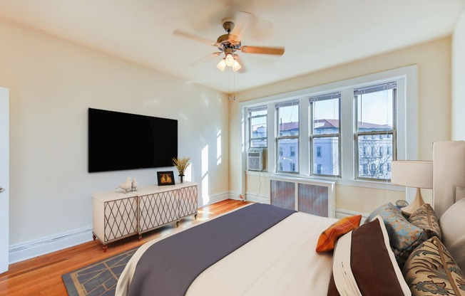 bedroom with bed, nightstand, tv, hardwood floors, ceiling fan and large windows at chatham courts apartments in washington dc