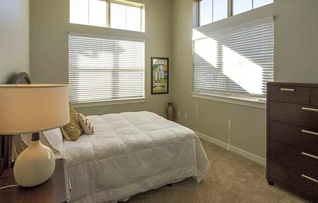 A bedroom with a white bed and a lamp on a table.