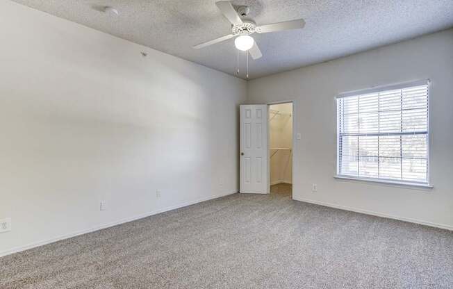 Spacious bedroom at Saxony at Chase Oaks Apartments in Dallas, TX, with white walls, neutral carpet, a ceiling fan, and a walk-in closet.