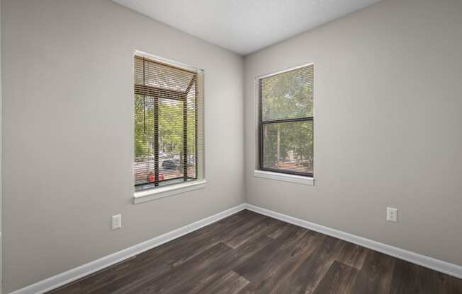 an empty room with wood floors and two windows