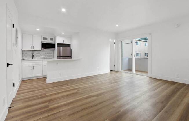 a living room and kitchen with white walls and wood floors