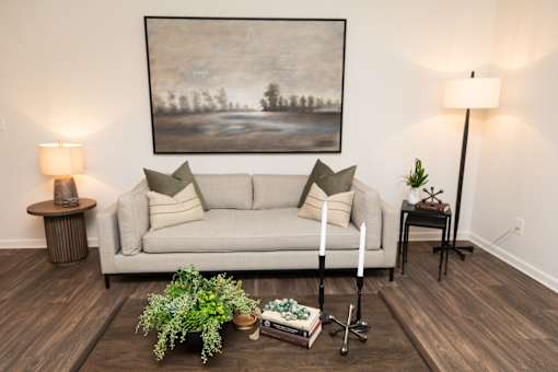 A living room with a grey couch, a painting on the wall, and a wooden floor.