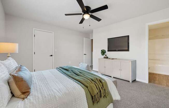 A bedroom with a bed, a ceiling fan, and a television.