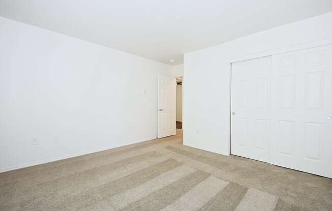 a bedroom with white walls and carpet and a door to a closet