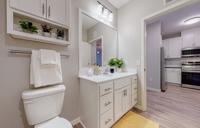 a bathroom with white cabinets and a white toilet next to a sink with a mirror above it