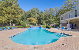 A large outdoor swimming pool surrounded by trees and lounge chairs.