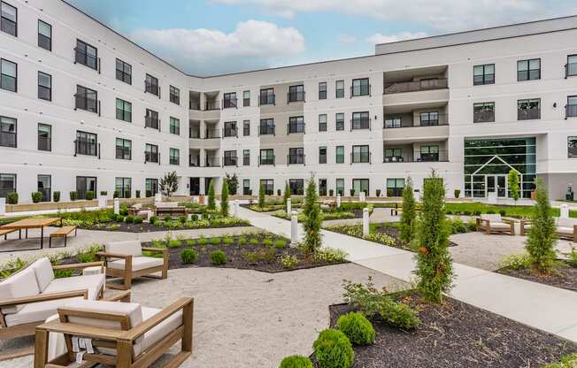 A courtyard with a white building in the background and a few trees and chairs in the foreground.