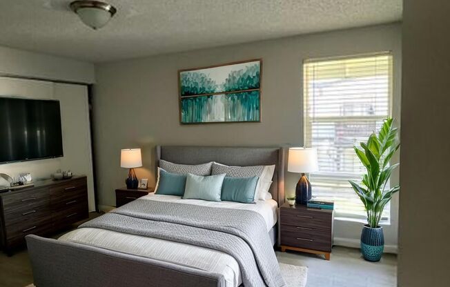 A bedroom with a large bed, a nightstand with a lamp, and a painting on the wall.