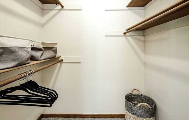 A small closet with clothes hanging and a basket on the floor.