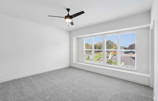 A room with a ceiling fan and a window showing a view of a residential area.