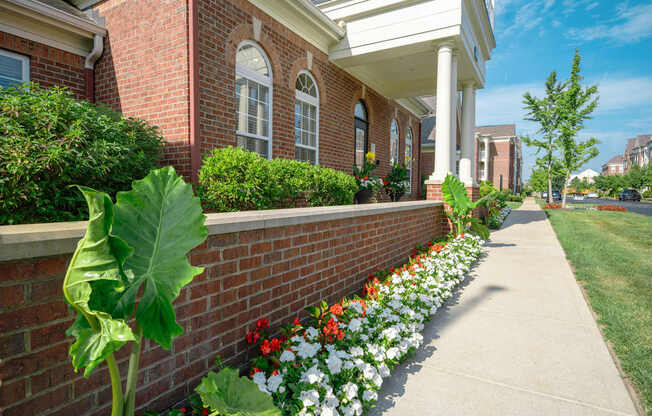 A brick building with a white porch and a flower bed in front.