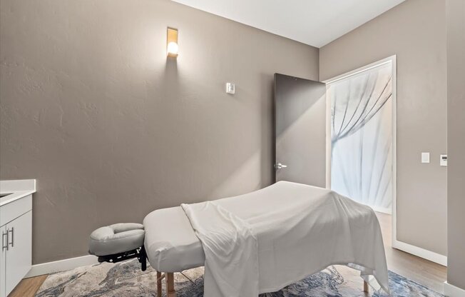 A room with a bed covered in a white sheet and a small ottoman.