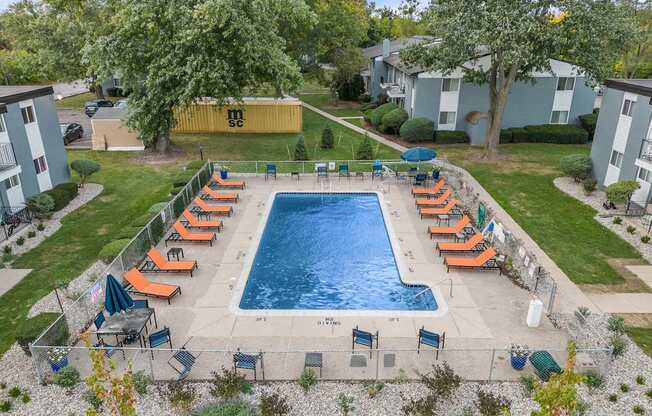 A pool surrounded by orange lounge chairs and green trees.