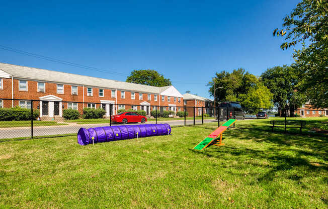 A playground with a purple slide and a red car parked in front of a brick building.