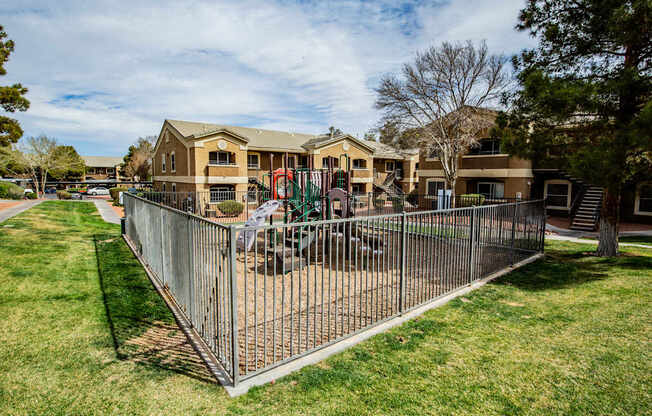 A playground area is enclosed by a fence in a grassy yard.