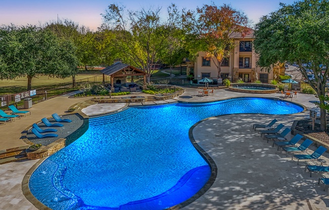A large blue pool surrounded by trees and a building.