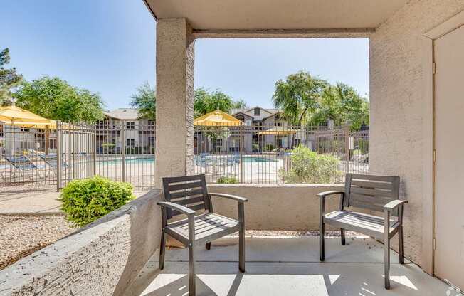 Two benches are placed in a concrete area with a view of a pool and trees.