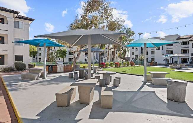 A sunny day at a park with concrete benches and umbrellas.