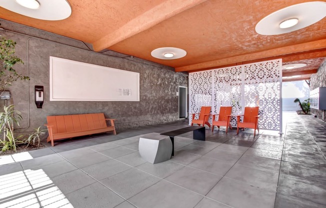 a lounge area with orange chairs and a whiteboard on the wall