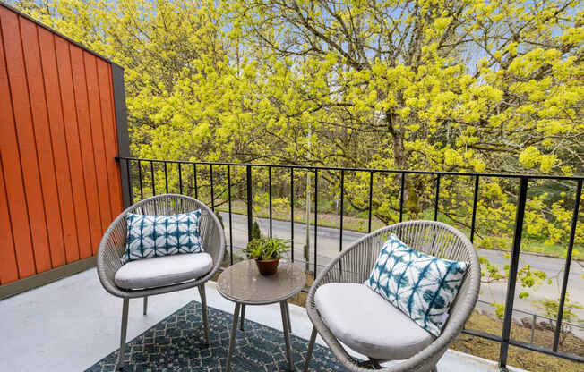 Two chairs and a table on a balcony with a view of trees.