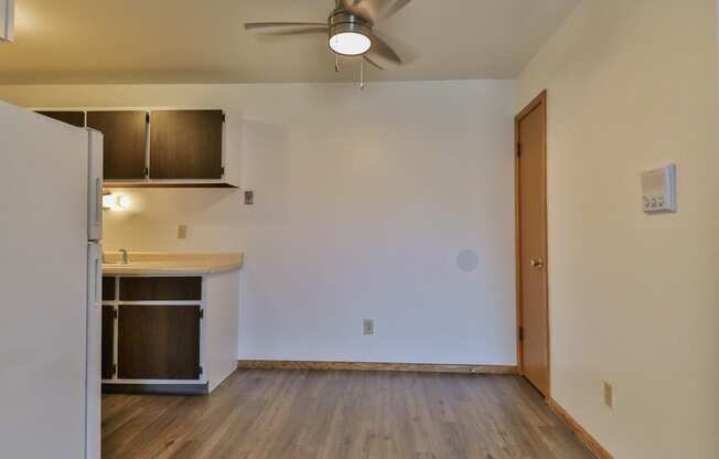 an empty living room with a kitchen and a ceiling fan