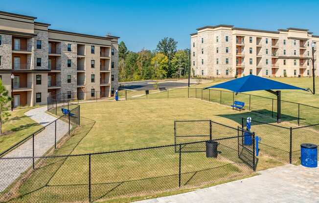 a fenced in dog park with agility courts in front of apartment buildings