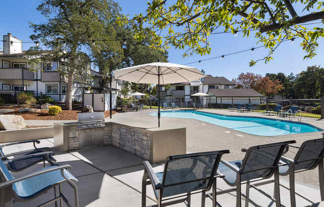 A pool surrounded by chairs and umbrellas with a house in the background.