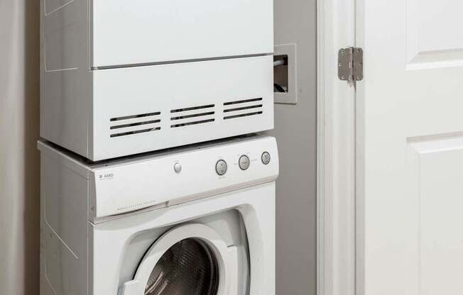 A white front loading washing machine is stacked on top of a smaller white dishwasher.