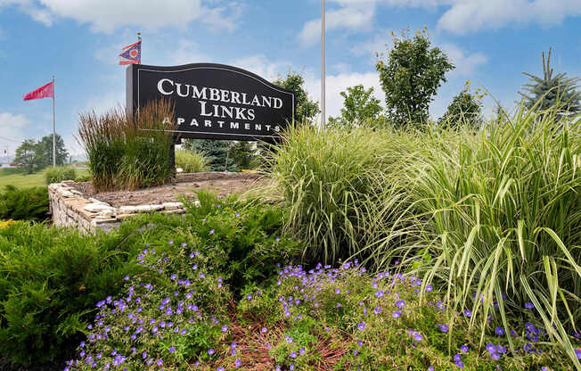 A sign for Cumberland Links Apartments is surrounded by greenery and flowers.