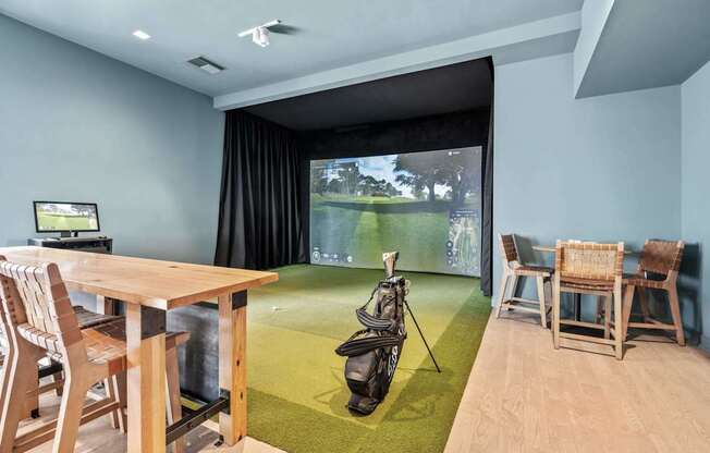 A room with a golf simulator and a table with chairs.