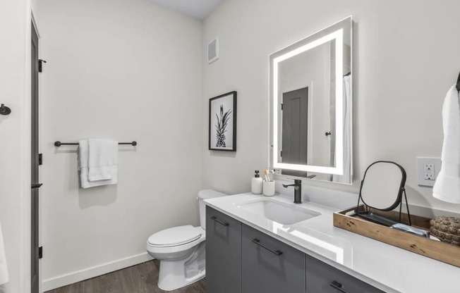 A white toilet is in a bathroom with a white sink and a mirror.