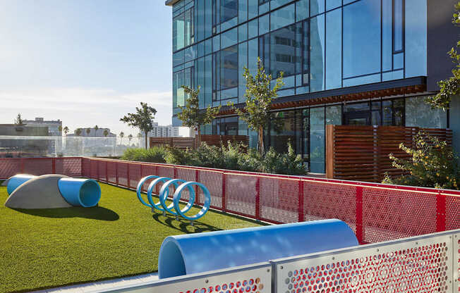A playground with a red fence and blue and grey slides.