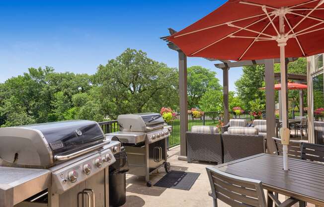 a patio with barbecue grills and tables with umbrellas