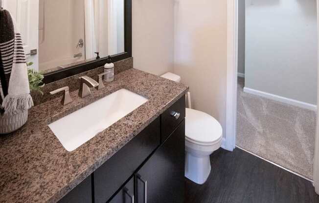 A bathroom with a sink, mirror, toilet and a shower.