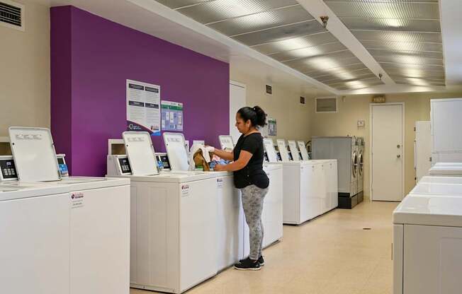 a woman standing at a line of washing machines in a laundromat at Hamilton Manor Apartments, Hyattsville, MD