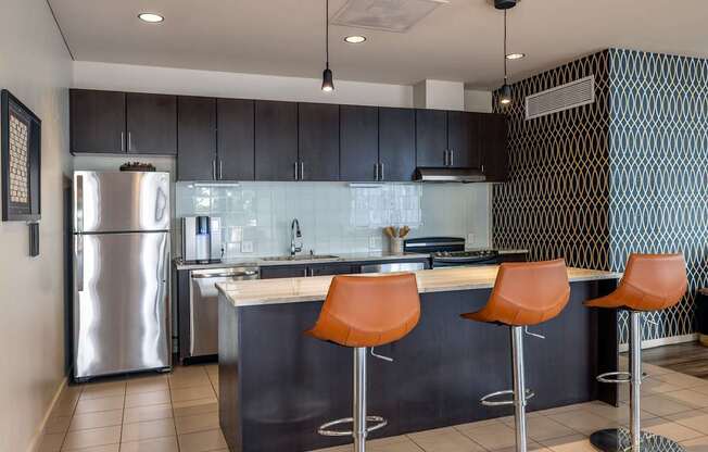 A modern kitchen with a stainless steel refrigerator and bar stools.