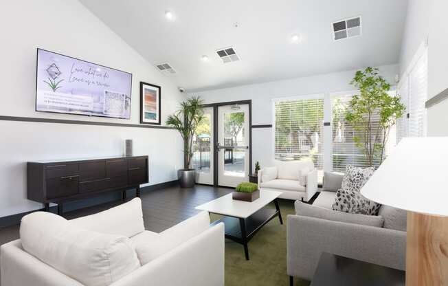 a living room with white couches and chairs and a tv on the wall