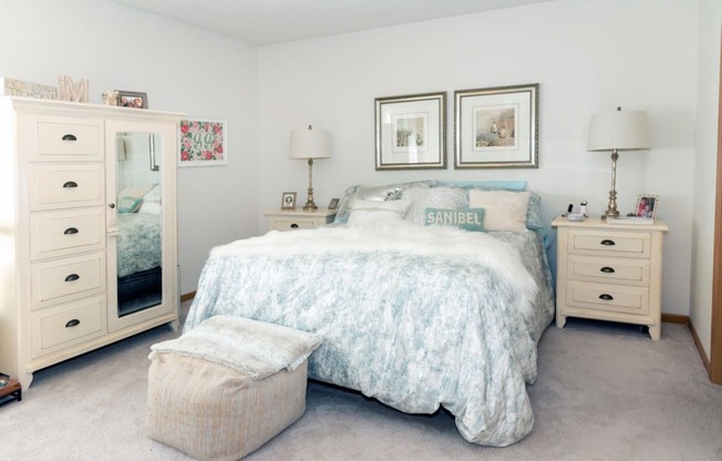 a bedroom with white walls and a bed with a white comforter and blue pillows
